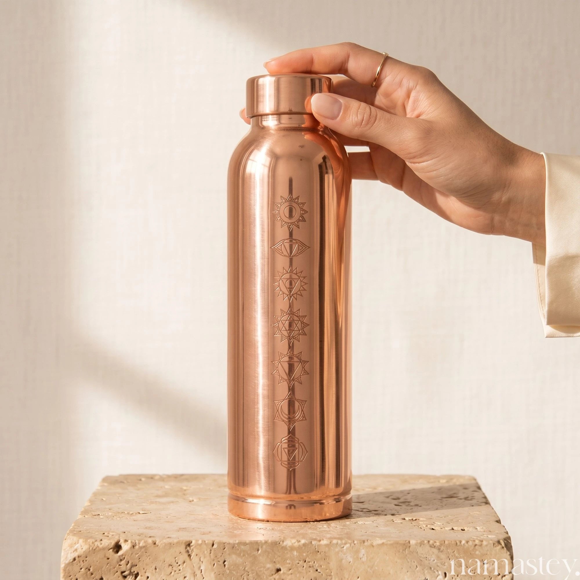 Hand placing the Chakra copper water bottle on a stone plinth