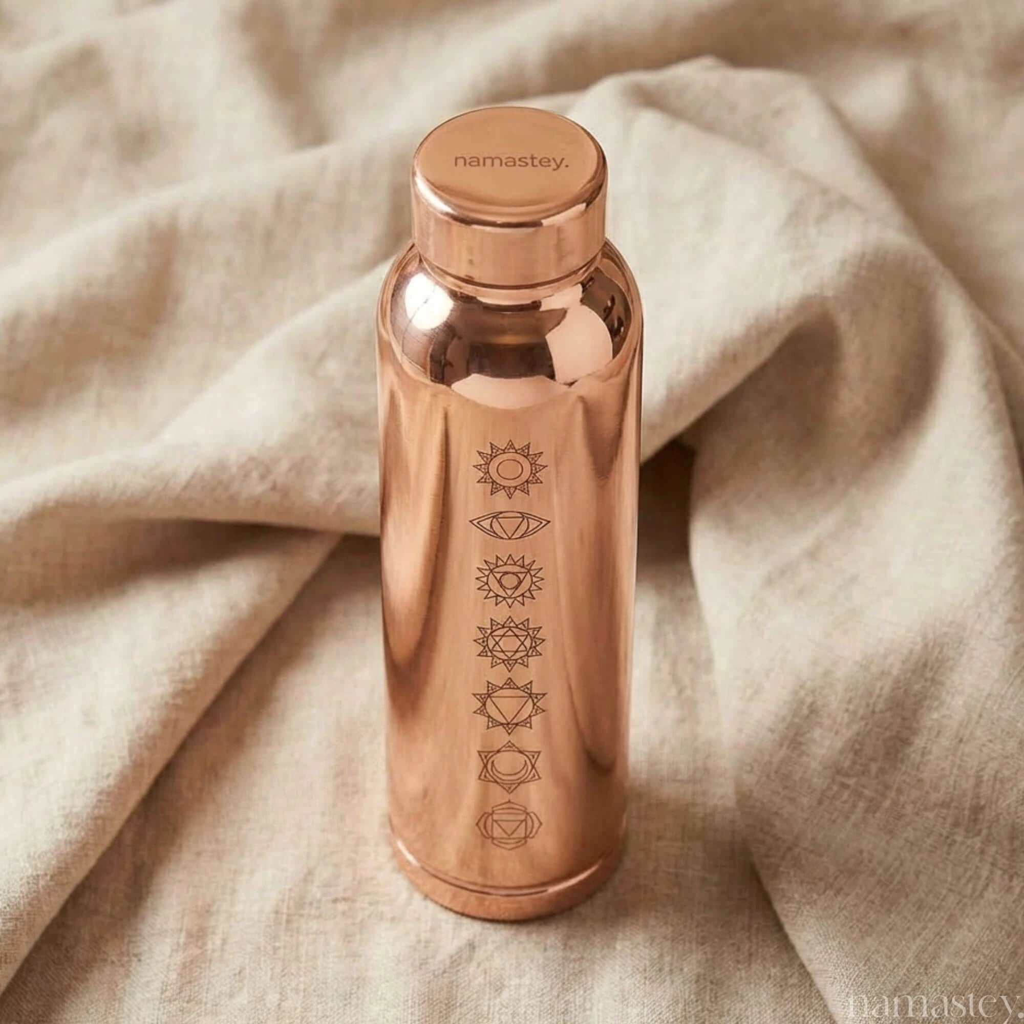 Chakra copper water bottle on linen with engraved Namastey lid and seven chakra symbols