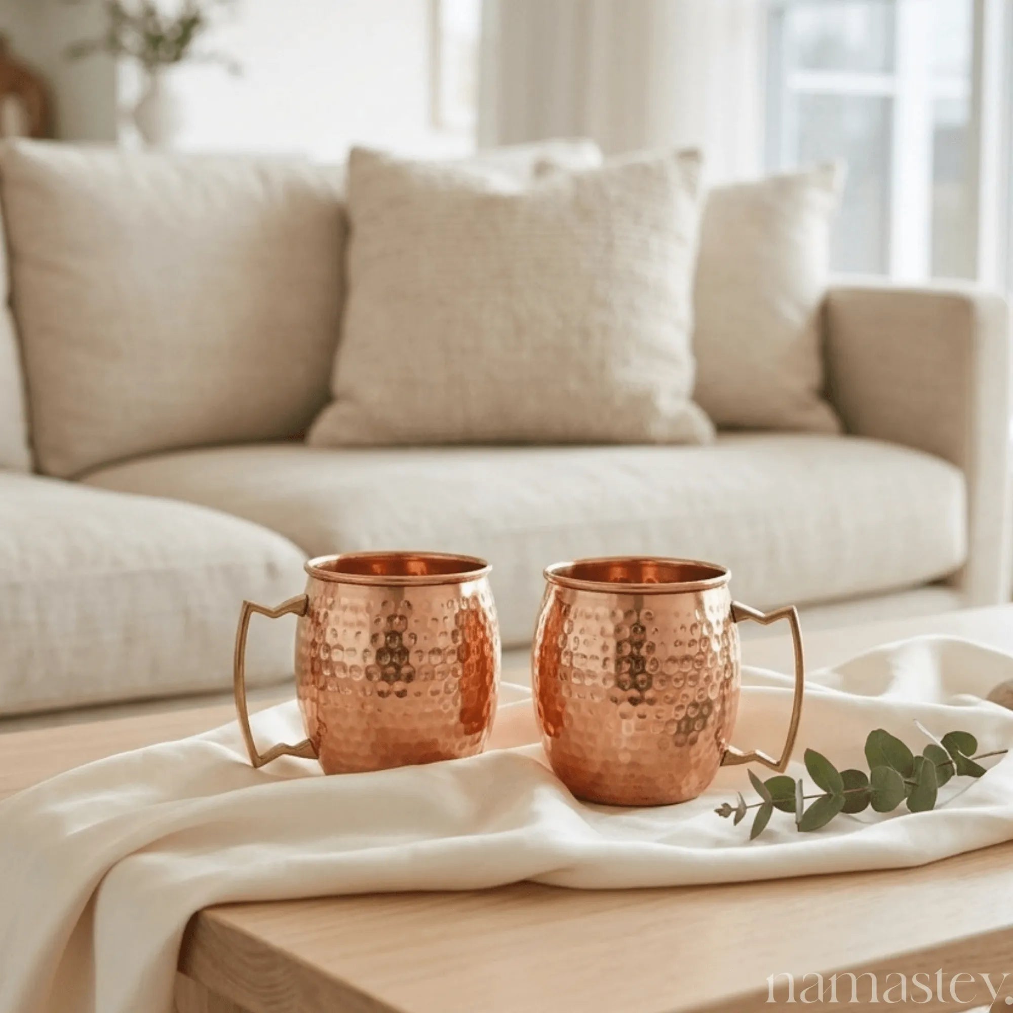 Two hammered copper mule mugs styled on a coffee table in a living room