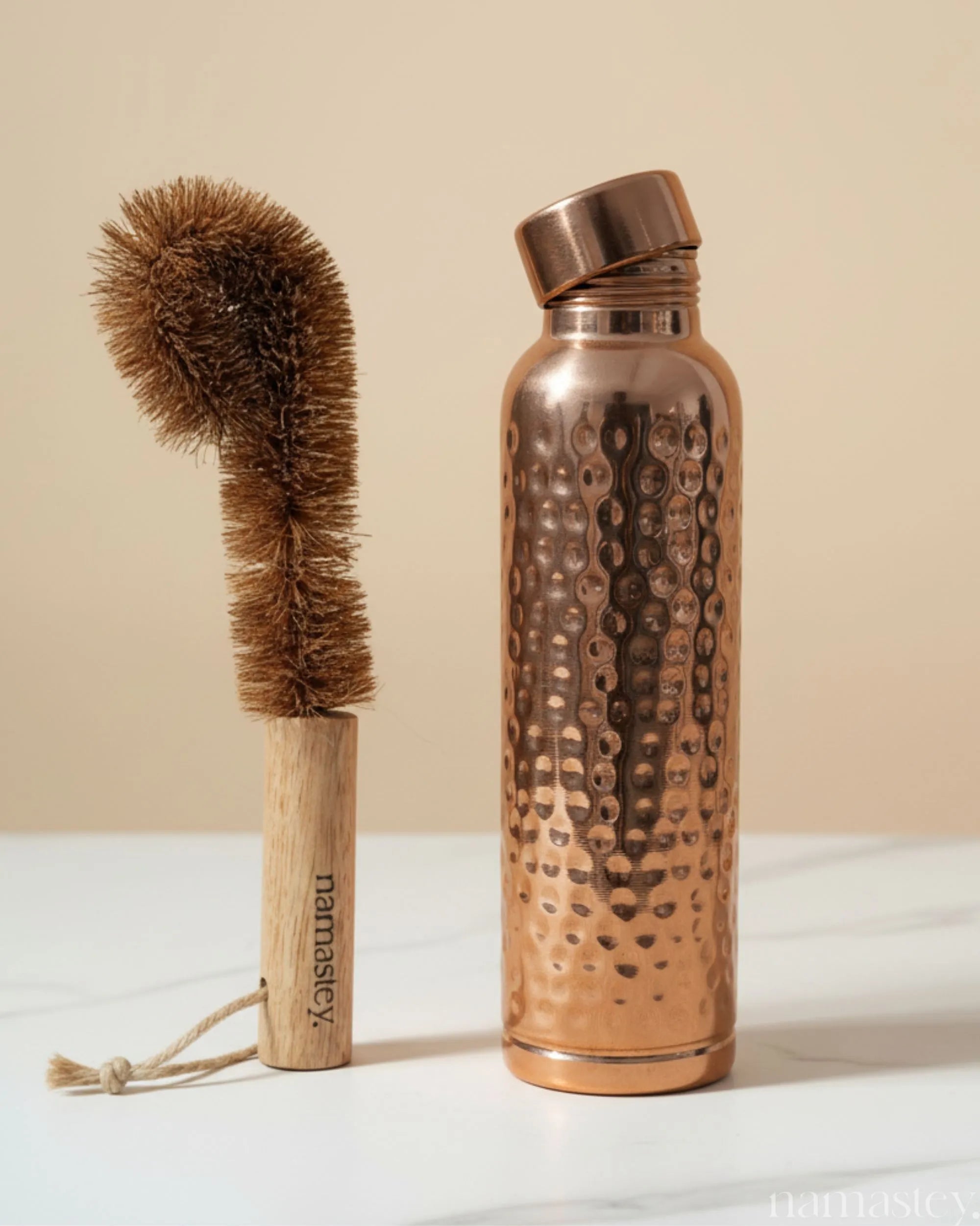 Classic hammered copper bottle beside a Namastey coconut-fibre cleaning brush